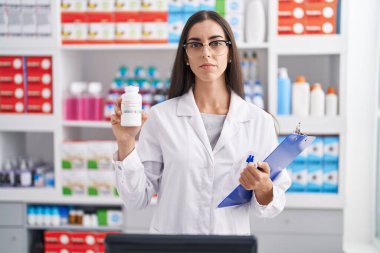 Eczanede çalışan esmer bir kadın elinde haplarla ciddi bir ifadeyle rahatlıyor. Basit ve doğal bir şekilde kameraya bakıyorsun.. 