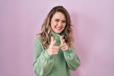 Young caucasian woman standing over pink background pointing fingers to camera with happy and funny face. good energy and vibes. 
