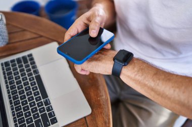 Orta yaşlı bir adam akıllı telefon kullanıyor ve terasta evi izliyor.