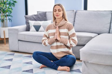 Yoga yapan genç bir kadın evde yerde oturuyor.