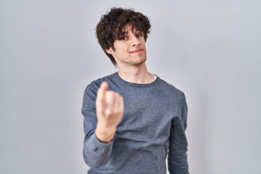 İzole edilmiş arka planda duran genç adam seni buraya davet ediyor. Elinle mutlu ve gülümseyen bir karşılama yap. 