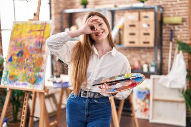 Sanat stüdyosunda elinde palet tutan beyaz bir kadın gülümsüyor. Mutlulukla gülümsüyor. 