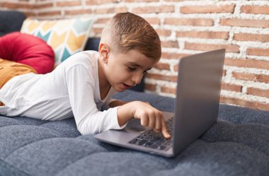 Adorable hispanic boy using laptop lying on sofa at home