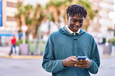 Sokakta akıllı telefon kullanan, kendinden emin gülümseyen Afrikalı Amerikalı bir adam.