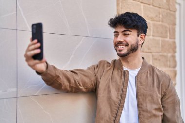 Young hispanic man smiling confident making selfie by the smartphone at street