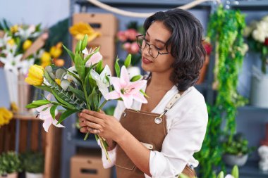 Young beautiful hispanic woman florist holding bouquet of flowers at flower shop