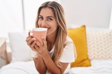 Genç sarışın kadın yatakta bir fincan kahve içiyor.