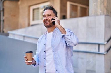 Young caucasian man talking on the smartphone drinking coffee at street