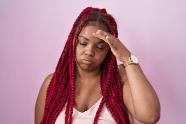Pembe arka planda örülü saçları olan Afrikalı Amerikalı bir kadın. Alnındaki bir sorun yüzünden endişeli ve stresli. Kriz konusunda endişeli. 