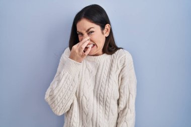 Genç esmer kadın mavi arka planda duruyor. Kokuşmuş ve iğrenç bir koku alıyor. Dayanılmaz bir koku. Kötü kokuyor. 