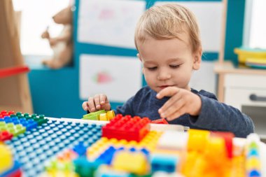 Anaokulunda duran sevimli sarışın çocuk inşaat bloklarıyla oynuyor.