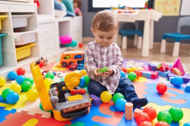 Anaokulunda yerde taşaklarıyla oynayan sevimli beyaz çocuk.