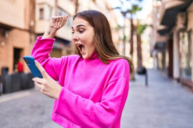 Gülümseyen genç bir kadın caddedeki akıllı telefondan konuşuyor.