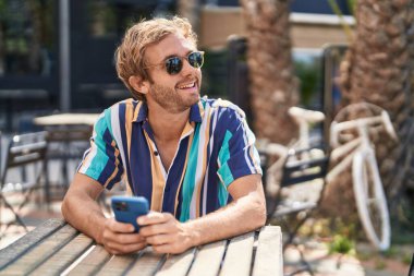 Kahve dükkanının terasında akıllı telefon kullanan genç bir turist.