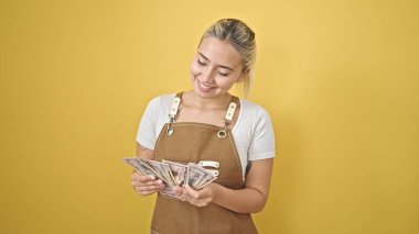 Önlük takan genç, güzel İspanyol kadın izole edilmiş sarı arka planda dolar sayıyor.