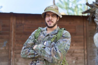 Asker üniforması giyen İspanyol genç adam parkta çapraz hareketlerle duruyor.