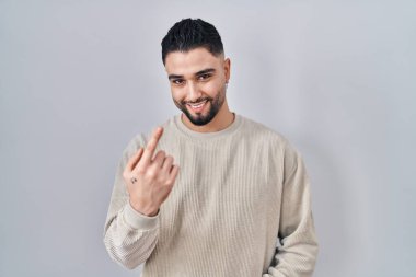 Soyutlanmış arka planda duran yakışıklı genç adam seni buraya davet ediyor. Elinle mutlu bir şekilde karşıla ve gülümse. 