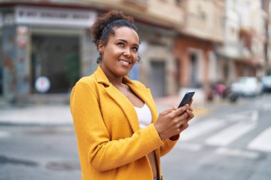 Afro-Amerikalı kadın sokakta akıllı telefon kullanarak kendine güveniyor.