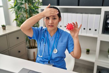 Elinde virüs oyuncağı tutan genç Latin doktor kadın. Eli kanlı, şaşırmış ve sinirli bir yüz. 
