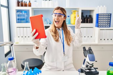 Laboratuvarda çalışan genç sarışın bilim kadını bir fikir ya da soruyla gülümsüyor ve mutlu bir yüzle işaret ediyor. 