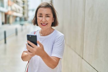 Sokakta akıllı telefon kullanan orta yaşlı bir kadın gülümsüyor.