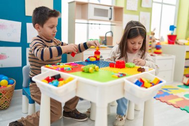 Anaokulundaki masada oturan sevimli kız ve oğlan inşaat bloklarıyla oynuyorlar.
