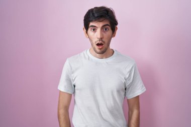 Young hispanic man standing over pink background afraid and shocked with surprise and amazed expression, fear and excited face. 