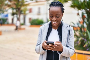 Afro-Amerikalı kadın parkta akıllı telefon kullanarak gülümsüyor.