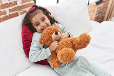 Sevimli İspanyol kız yatak odasında uzanmış oyuncak ayıya sarılıyor.