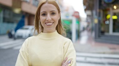 Sokakta kolları çapraz duran genç sarışın kadın.