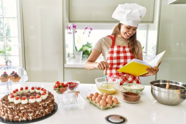 Genç ve güzel İspanyol kadın yemek tarifi kitabı okuyor. Mutfakta yumurta karıştırıyor.