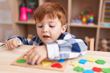 Sınıftaki masada oturan, matematik bilmecesiyle oynayan sevimli çocuk.