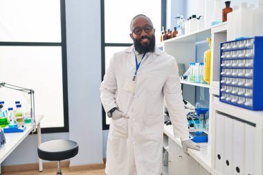 Laboratuvarda duran, bilim adamı üniforması giyen genç Afro-Amerikan adam.