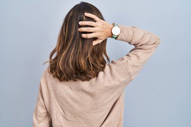 Young woman standing over isolated background backwards thinking about doubt with hand on head 