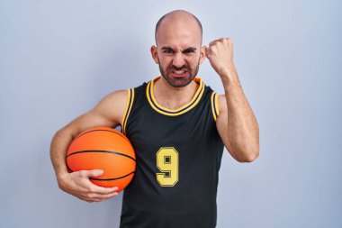 Sakallı, sakallı, basketbol forması giyen kızgın ve kızgın bir şekilde topu tutan ve öfkeyle bağıran genç, kel bir adam. öfke ve agresif konsept. 