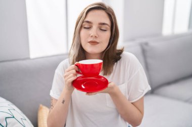 Evdeki kanepede kahve içen genç bir kadın.