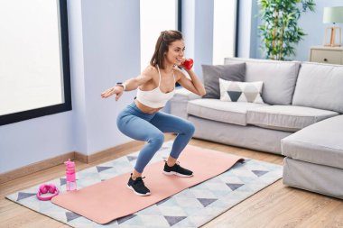 Genç ve güzel İspanyol kadın evde dambıl kullanarak bacak egzersizi yapıyor.