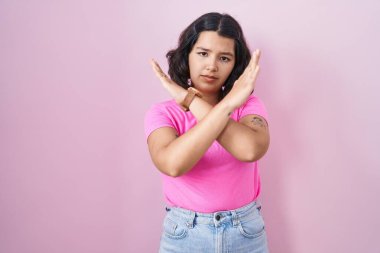 Young hispanic woman standing over pink background rejection expression crossing arms doing negative sign, angry face 