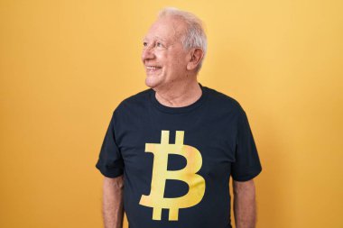 Bitcoin tişörtlü, gri saçlı son sınıf öğrencisi yüzünde gülümsemeyle yan yana bakıyor, doğal bir ifade. Kendinden emin gülen. 