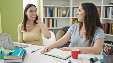 Kütüphane üniversitesinde akıllı telefon sohbeti için rahatsız edici iki kadın.