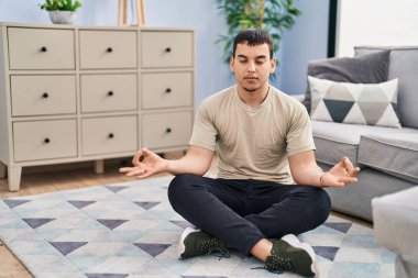 Yoga egzersizi yapan genç bir adam evde yerde oturuyor.