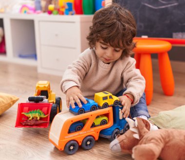 Anaokulunda yerde oturan sevimli İspanyol çocuk araba oyuncağıyla oynuyor.