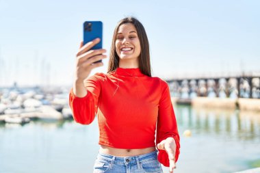 Genç, güzel, İspanyol bir kadın, gülümsüyor. Sahilde kendine güvenen bir telefon görüşmesi yapıyor.
