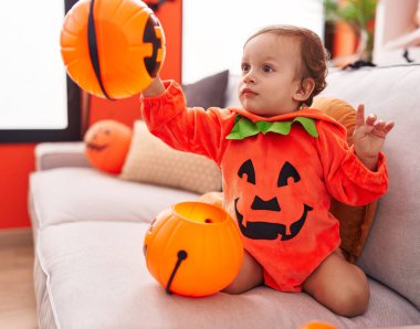 Evdeki kanepede oturan balkabağı kostümü giyen sevimli İspanyol çocuk.