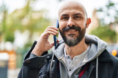 Genç kel adam gülümsüyor. Kendine güveni tam. Akıllı telefondan konuşuyor.