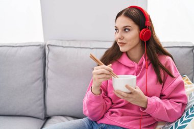 Young woman listening to music eating chinese food at home