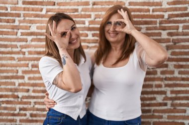 Latin kökenli anne ve kız günlük beyaz tişörtler giyiyorlar. El hareketleriyle gülümsüyorlar. Gözleri, mutlu yüzleriyle parmaklarından bakıyor.. 