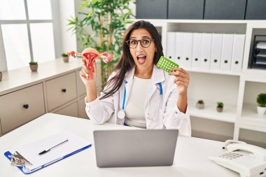 Genç İspanyol doktor kadın anatomik kadın organı ve doğum kontrol hapları tutuyor. Çılgınlığı kutluyor ve başarıyı hayretle kutluyor.. 