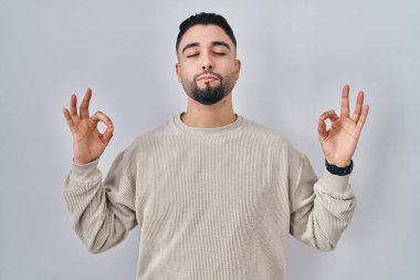 Tecrit edilmiş arka planda duran genç yakışıklı adam rahatlamış ve parmaklarıyla meditasyon hareketi yaparken gözleri kapalı gülümsüyor. yoga konsepti. 