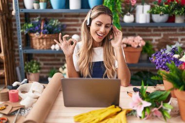 Young blonde woman working at florist shop doing video call doing ok sign with fingers, smiling friendly gesturing excellent symbol 